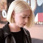 Person with blonde hair wearing black jacket.